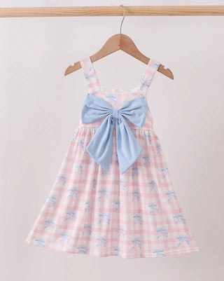 A pink and white gingham dress with a light blue bow on the bodice and small blue bow prints, hanging on a wooden hanger against a light beige wall.