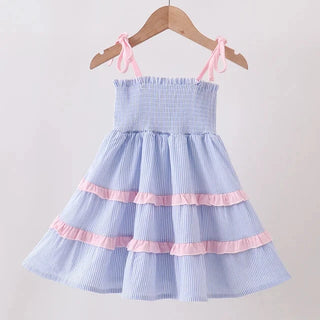 A light blue and white vertically striped baby dress with pink ruffle accents and tie straps, hanging on a wooden hanger against a plain white background.