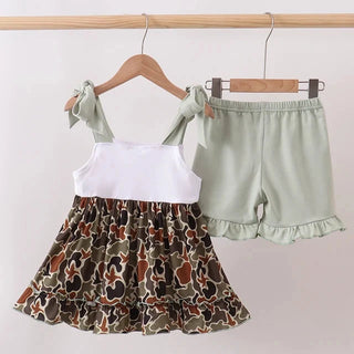A toddler girl's two-piece outfit set hanging on wooden hangers against a plain light background. The set includes a sleeveless top with a solid white upper section and a tiered skirt in a brown, beige, and black camouflage pattern, paired with sage green ruffled shorts.