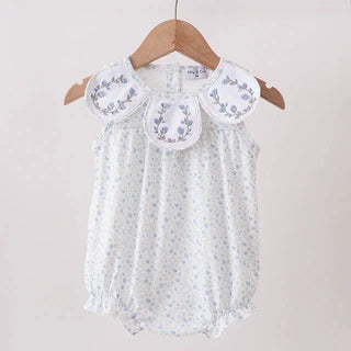 A sleeveless baby romper with a white base and light blue floral print, featuring a decorative embroidered collar, hanging on a wooden hanger from a wooden clothes rack against a plain light background.
