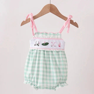 A baby romper with a mint green and white gingham pattern, featuring a white smocked chest panel with pink trim and small embroidered details, hanging on a wooden hanger.