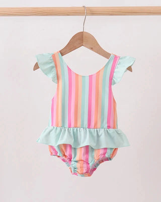 A baby girl's one-piece swimsuit with pastel vertical stripes in mint green, pink, orange, and yellow, featuring ruffle details on the shoulders and a ruffled hem, hanging on a wooden hanger.