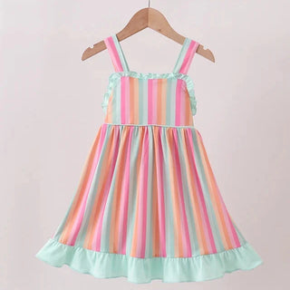 A toddler girl's sleeveless dress with pastel rainbow vertical stripes and mint green ruffled trim, hanging on a wooden hanger from a wooden clothes rack against a light beige wall.