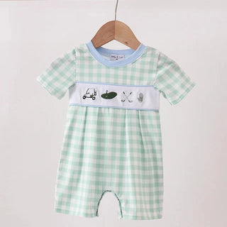 A baby short-sleeve romper in a light green and white gingham pattern, hanging on a wooden hanger. The romper features a light blue collar, a white horizontal band across the chest with small golf-themed illustrations (cart, golf ball, clubs, tees), and a matching white hem.