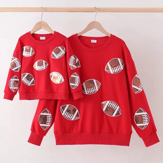 A matching red children's sweatshirt set hanging on wooden hangers against a plain light wall. The set includes a short-sleeve top and a long-sleeve sweatshirt, both printed with brown and white football motifs.