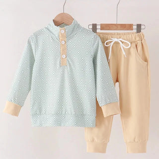 A two-piece children's outfit set hanging on wooden hangers against a plain light background. The set includes a long-sleeve mock-neck top in pale mint green with a geometric diamond pattern and beige button placket, paired with beige jogger pants featuring a white drawstring waist.
