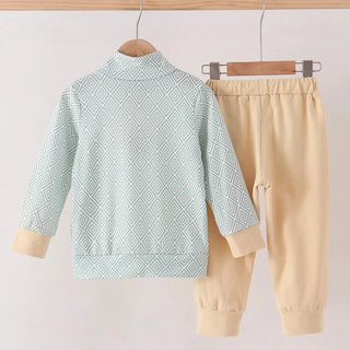 A two-piece children's outfit hanging on wooden hangers against a plain light background. The set includes a long-sleeve mock-neck jacket in pale mint green with a repeating geometric diamond pattern and beige cuffs, paired with beige jogger pants with elastic waist and cuffs.
