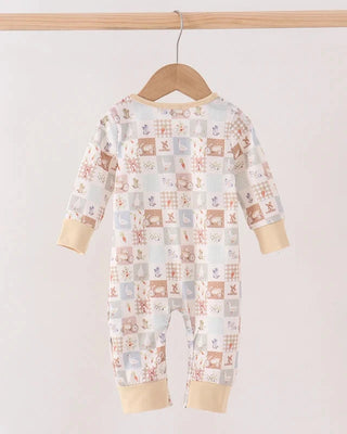 A baby long-sleeve footless jumpsuit with a patchwork animal print, hanging on a wooden hanger from a wooden clothes rack against a plain light background.