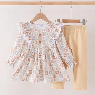 A toddler girl's two-piece outfit hanging on wooden hangers against a plain light background. The set includes a long-sleeve ruffled blouse with a patchwork print in beige, white, and muted orange-brown, paired with solid light beige leggings.