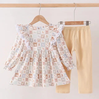 A toddler girl's two-piece outfit set hanging on wooden hangers against a plain white wall. The set includes a long-sleeve ruffle-trimmed top with a multicolor patchwork print on a white base, and solid light beige leggings.