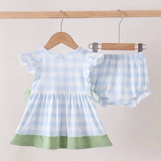 A baby girl's two-piece outfit set consisting of a light blue and white gingham dress with a sage green hem and matching gingham bloomers, hanging on wooden hangers from a wooden clothes rack.