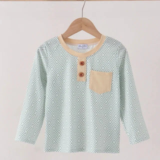 A long-sleeve t-shirt with a light green and white geometric diamond pattern, featuring a beige crew neck, a beige chest pocket, and two brown buttons, hanging on a wooden hanger.