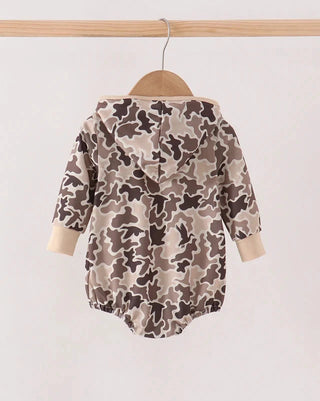 A baby long-sleeve romper with a brown, beige, and gray camouflage pattern, hanging on a wooden hanger from a light wood rod against a plain off-white background.