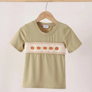 A short-sleeve boy tee in sage green hanging on a wooden hanger. The shirt features a horizontal decorative band across the chest with a cream-colored knit pattern and a row of small orange embroidered pumpkins.