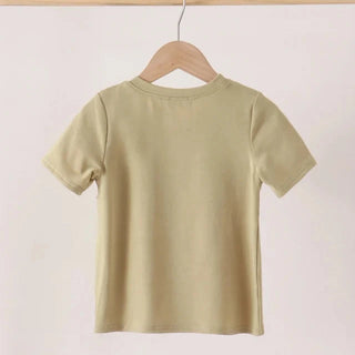 A light olive green short-sleeve t-shirt hanging on a wooden hanger from a wooden clothes rack against a plain off-white background.