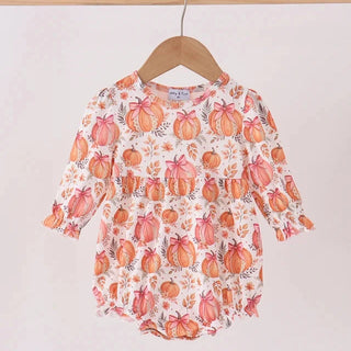 A baby girl’s  long-sleeve romper with a pumpkin print, hanging on a wooden hanger from a wooden clothes rack against a plain off-white wall.