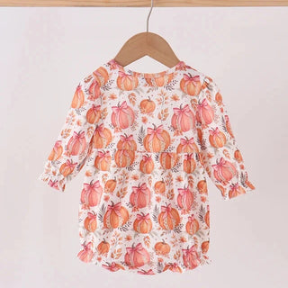 A baby girl's long-sleeve top with a pumpkin print, hanging on a wooden hanger from a light wood clothing rack against a plain off-white wall.