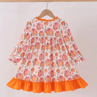 A long-sleeve children's dress hanging on a wooden hanger against a plain light background. The dress has an allover pumpkin print in orange, pink, and white, with a solid bright orange ruffled hem and neckline trim.