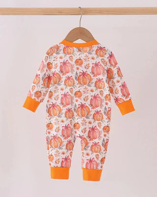 A baby long-sleeve footless one-piece jumpsuit with an all-over orange and pink pumpkin print on a white background, featuring bright orange cuffs and leg hems, hanging on a wooden hanger from a wooden rod.
