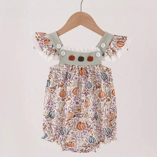 A baby girl's short-sleeve romper with a fall harvest pumpkin print, hanging on a wooden hanger against a plain off-white wall.