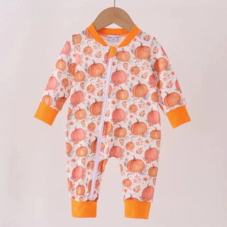 A baby long-sleeve footless one-piece sleeper with an orange and white pumpkin print, hanging on a wooden hanger against a light beige background.