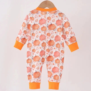 A baby long-sleeve footless jumpsuit with an orange and white pumpkin print, hanging on a wooden hanger from a light wood bar against a plain off-white background.