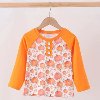 A children's long-sleeve henley top hanging on a wooden hanger against a plain light background. The shirt has bright orange sleeves and collar, with a front panel covered in an allover pumpkin print on a white base.