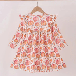 A long-sleeve dress with a pumpkin print, hanging on a wooden hanger from a light wood rod against a plain off-white wall.