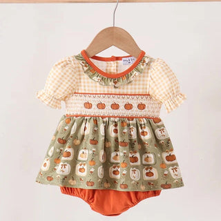 A baby girl's short-sleeve smocked dress with a pumpkin print skirt and orange bloomers, hanging on a wooden hanger against a white background.