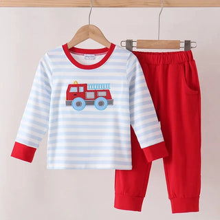 A children's two-piece pants set hanging on wooden hangers against a light beige wall. The set includes a long-sleeve top with white and light blue horizontal stripes, red collar, cuffs, and a red fire truck graphic on the chest, paired with solid red pants.