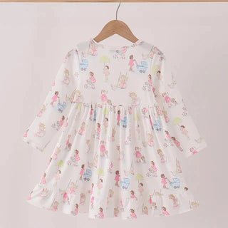 A long-sleeve baby dress with a white base and a colorful cartoon print of children, hanging on a wooden hanger against a plain light background.