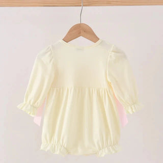 A pale yellow baby top with puff sleeves and ruffled trim, hanging on a wooden hanger against a light beige background.