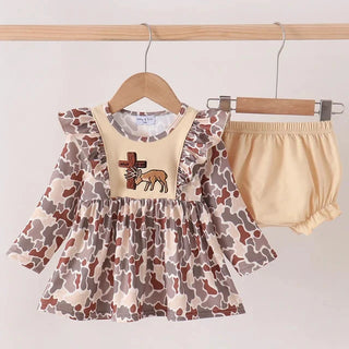 A baby girl's two-piece outfit hanging on wooden hangers against a plain light background. The set includes a long-sleeve ruffled dress with a beige, brown, and gray camouflage pattern and a brown cross with a cow graphic on the chest, paired with matching beige bloomers.