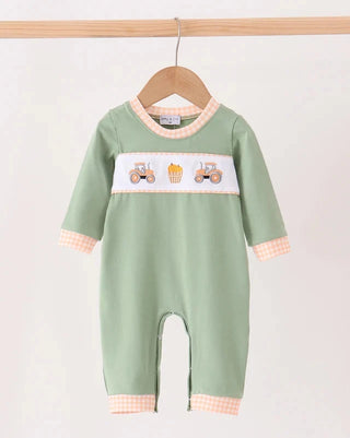 A sage green baby romper hanging on a wooden hanger against a light background. The romper features a white chest panel with illustrations of tractors and a bucket of fries, finished with peach and white gingham trim on the collar, cuffs, and leg openings.