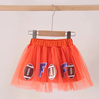 An orange tulle tutu skirt with football patches and  letter F, hanging from a wooden hanger on a clothing rack against a plain light background.