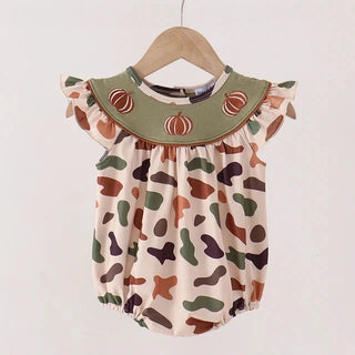 A baby romper with a camouflage pattern in shades of green, brown, and beige, featuring a solid olive green ruffled collar decorated with embroidered orange and white pumpkins. The romper is displayed on a wooden hanger against a plain off-white background.
