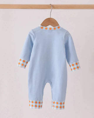 A baby long-sleeve footless romper in light blue, hanging on a wooden hanger. The garment features orange and white checkered trim at the crew neck, cuffs, and ankle openings.