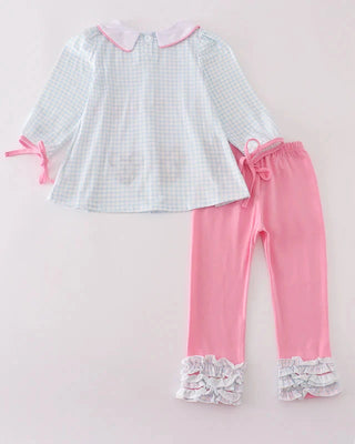 Children's outfit with checkered top and pink pants on a light pink background