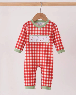 A baby long-sleeve romper in a red and white gingham check pattern with sage green trim, hanging on a wooden hanger against a light beige background.
