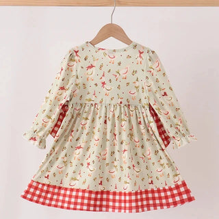 A long-sleeve dress with a cream background and a red and green holiday print, featuring a red and white gingham check hem, hanging on a wooden hanger against a plain white wall.
