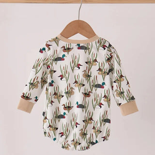 A baby long-sleeve romper with an all-over duck and reeds print, hanging on a wooden hanger from a light wood rod against a plain off-white background.