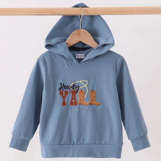 A light blue kids' hooded sweatshirt hanging on a wooden hanger from a wooden rod, featuring a 'Husky Yell' graphic with cowboy boots and a lasso design on the chest.