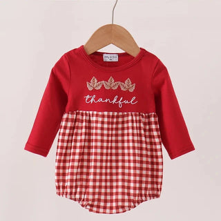 A baby girl's long-sleeve romper hanging on a wooden hanger against a light beige background. The top is solid red with a 'thankful' script and gold leaf embroidery, while the bottom half features a red and white gingham check pattern.