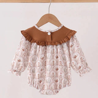A baby romper with a brown ruffled Peter Pan collar and a light pink patterned body, hanging on a wooden hanger against a plain light background.