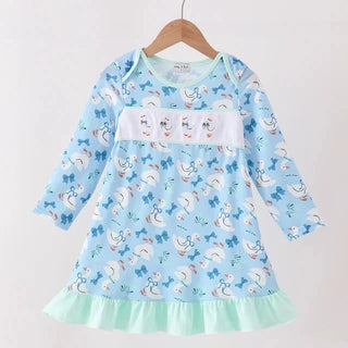 A light blue long-sleeve dress with a white smocked chest panel and an all-over goose print, hanging on a wooden hanger against a plain white background.