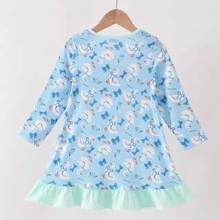 A light blue long-sleeve dress with a playful goose and bow print, featuring a mint green ruffled hem, hanging on a wooden hanger against a plain light background.