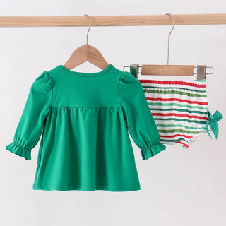 A toddler girl's two-piece outfit hanging on wooden hangers from a clothing rack. The set includes a bright green long-sleeve top with ruffled cuffs and a matching green bow on the side, paired with white smocked bloomers featuring red and green stripes.
