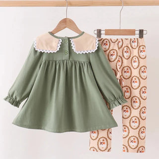 A toddler girl's two-piece outfit set hanging on wooden hangers against a plain white background. The set includes an olive green long-sleeve dress with a cream-colored Peter Pan collar with white lace trim, and matching beige pants with a brown and red floral oval pattern.