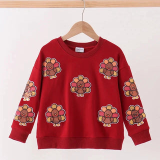 A red crewneck sweatshirt with a repeating pattern of embroidered turkeys, hanging on a wooden hanger from a light wood rod against a plain white background.