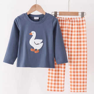 A children's two-piece clothing set hanging on a wooden hanger bar. The set includes a slate blue long-sleeve top with a white goose applique on the front, and matching orange-and-white gingham check pants.